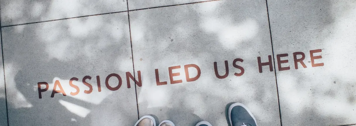 “Passion led us here” painted on a sidewalk, next to two pairs of sneakers