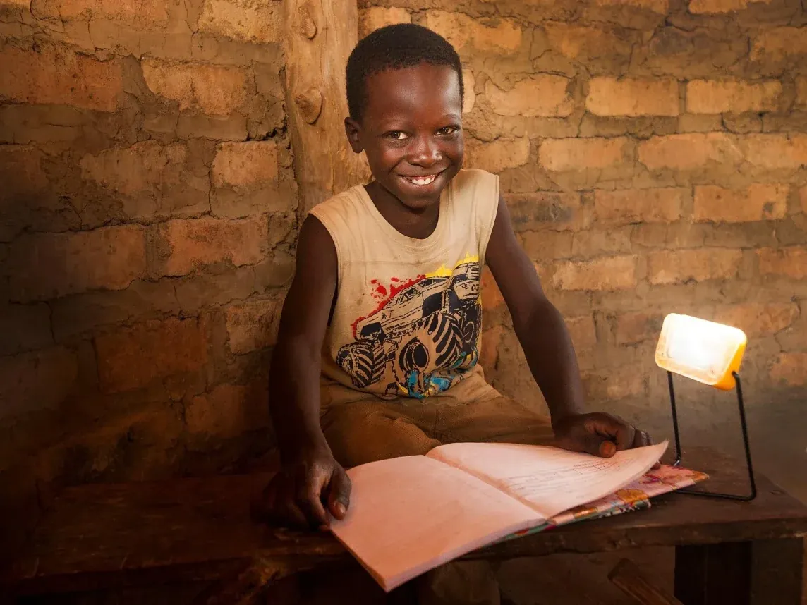Un garçon souriant fait ses devoirs à la lumière d’une lampe solaire